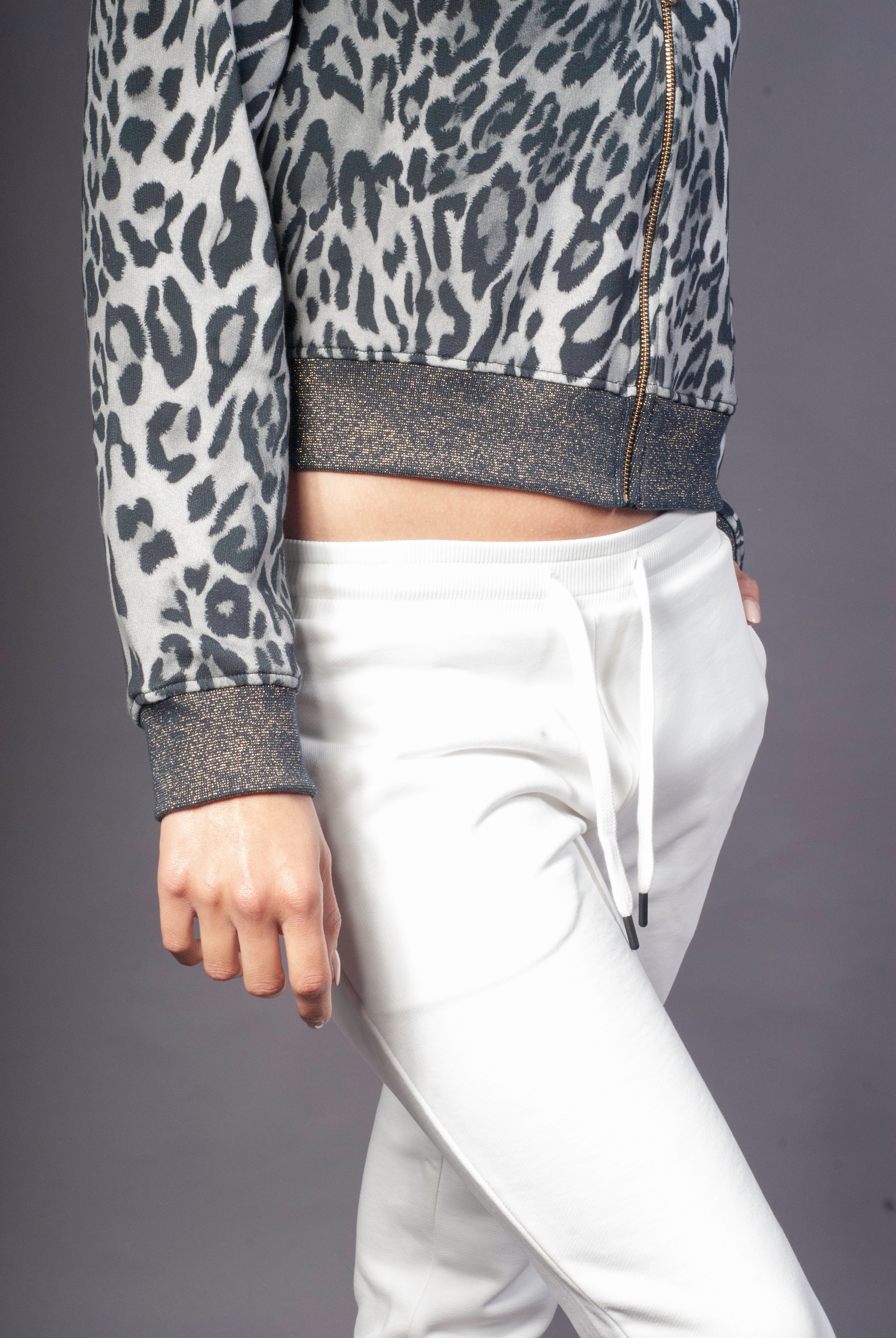 Close-up of a person wearing a leopard-print jacket with glittery cuffs and white drawstring pants.