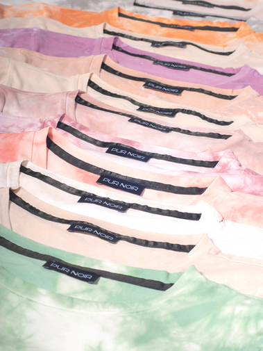 Overlapping pastel tie-dye garments with repeated black “PUR NOIR” collar labels.
