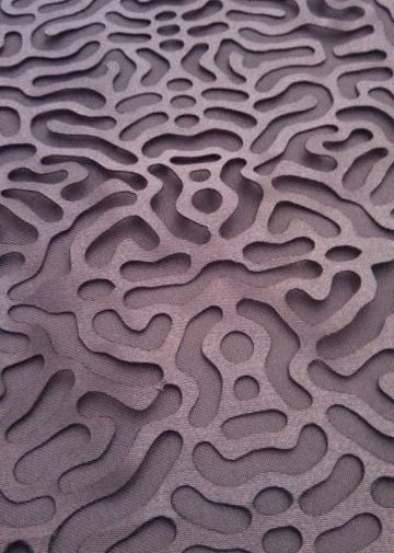 Close-up of a mauve-gray surface with dense, raised maze-like grooves and rounded organic shapes.