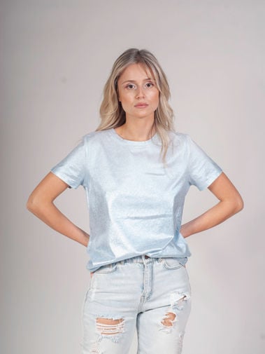 Woman in a pale blue T-shirt and ripped light-wash jeans standing with her hands on her hips.