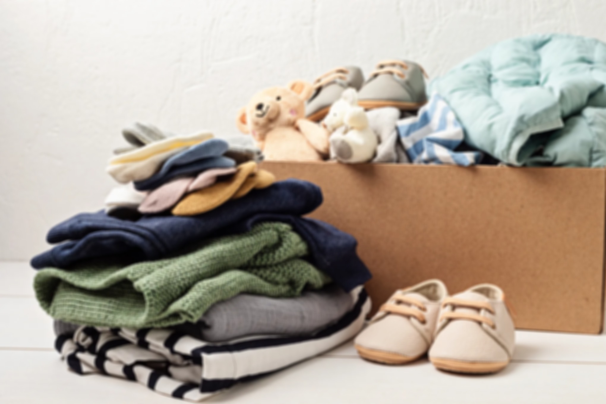 Folded clothes, beige shoes, and stuffed animals are arranged beside an open cardboard storage box.