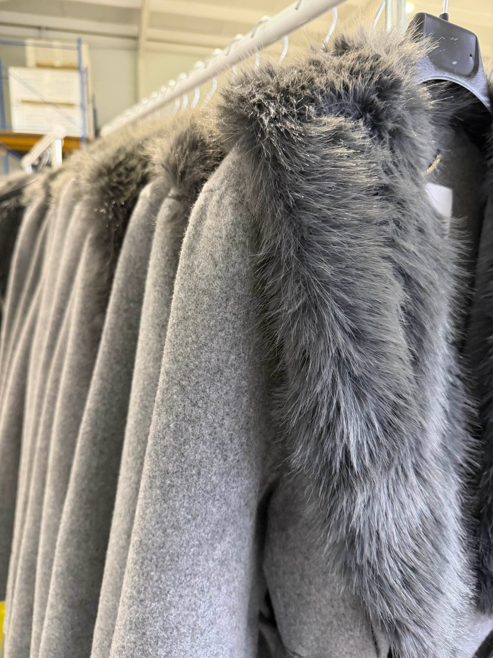 Close-up of gray coats with shaggy gray fur-like trim hanging on a clothing rack.