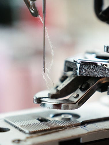 Close-up of a sewing machine needle, thread, presser foot, and grooved metal needle plate.