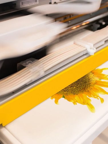 Close-up of a large-format printer producing a sunflower image on white paper.