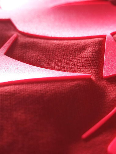 Close-up of layered red fabric with woven texture, angular folds, and bright reflective highlights.